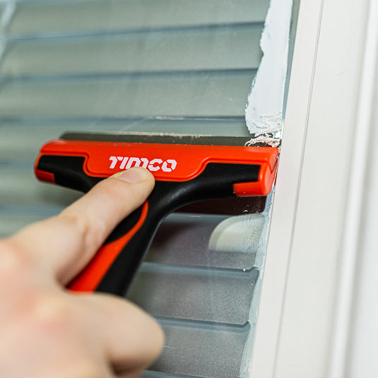 scraper removing sealant from glass windows